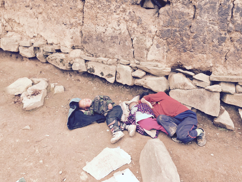 “小弟弟躺在門前鋪的一件衣服上,鼓起高高的肚皮,照顧他的大妹對(duì)著他的肚臍吹氣。”(作者供圖)